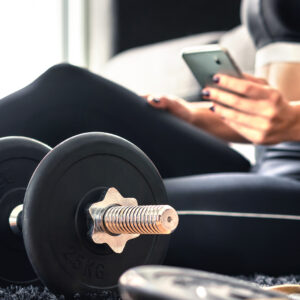 Image of a woman in fitness clothes next to some weights looking at her cell phone